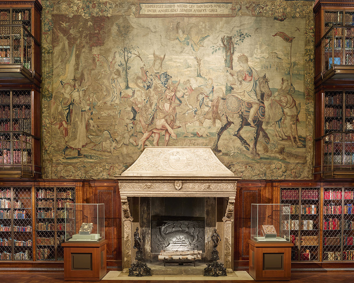 Tapestry hanging over a fireplace with book shleves on either side.