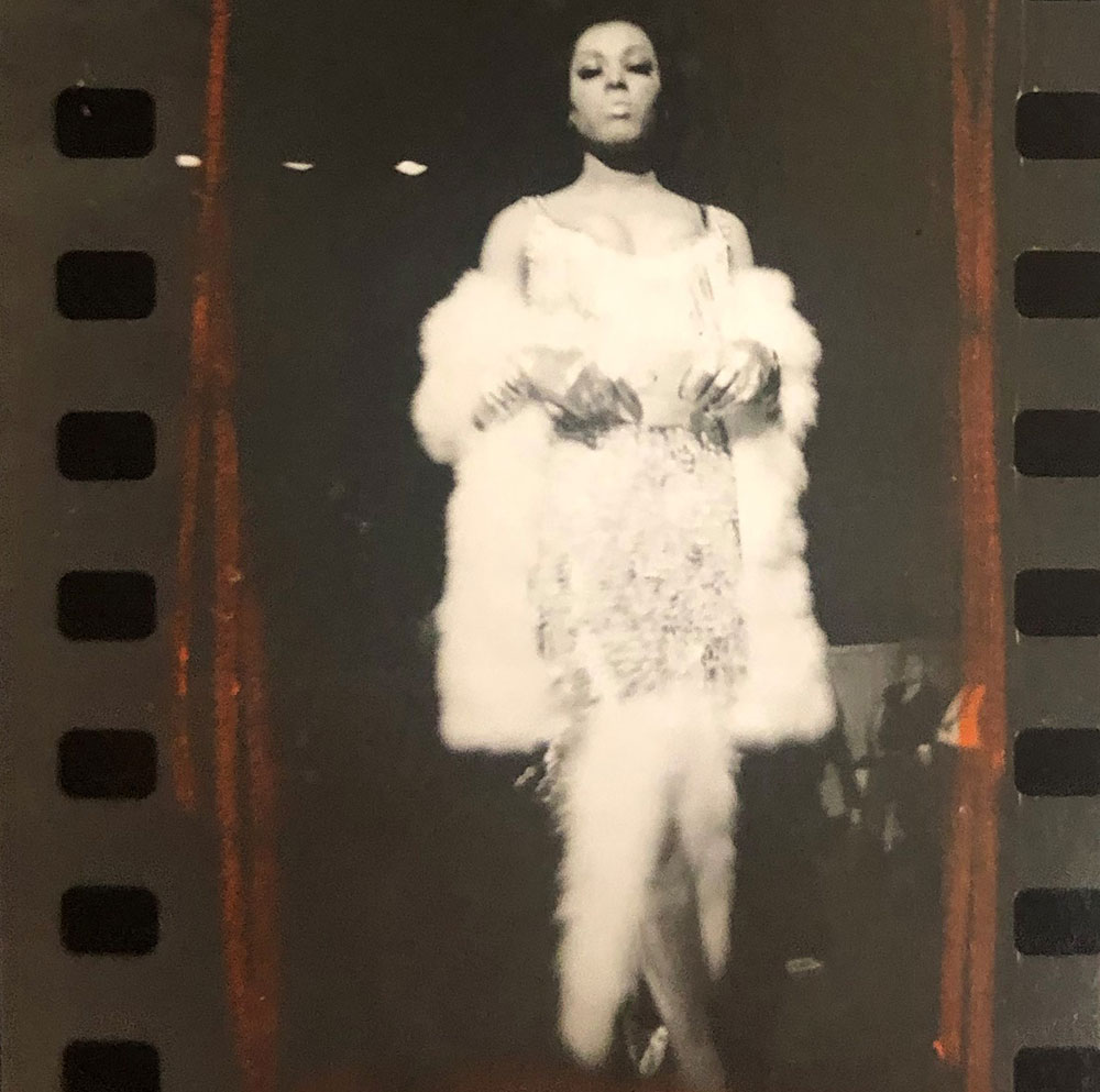 A black and white image selected from a contact sheet and marked with a red pencil. The image shows a full body shot of Crystal LaBeija in front of a black background, wearing a white evening gown with a white marabou bottom, long white gloves, and a white fur stole.