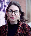 Color photograph of Madison Schindele showing head and shoulders and  wearing glasses, earrings, and black and red top.