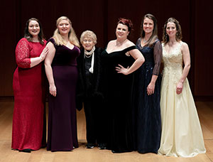 Five women in evening gowns posing for camera.