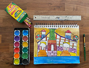 Colorful drawings on wood background with watercolor paint palettes and crayon box to the side.