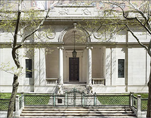 Exterior of J. Pierpont Morgan's Library building constructed of white marble columns and archway over fromt door and two statues of lionsnesses laying down on either side of stairs.