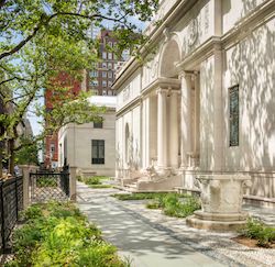 Photograph showing J. Pierpont Morgan's Library white marble building with columns and tress and plants in garden.