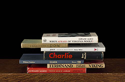 Color photo of a small stack of books sitting on a wooden surface with a black background.
