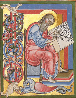 Illumination of seated scribe with long brown hair and beard, wearing red and bkue robes, holding a manuscript.