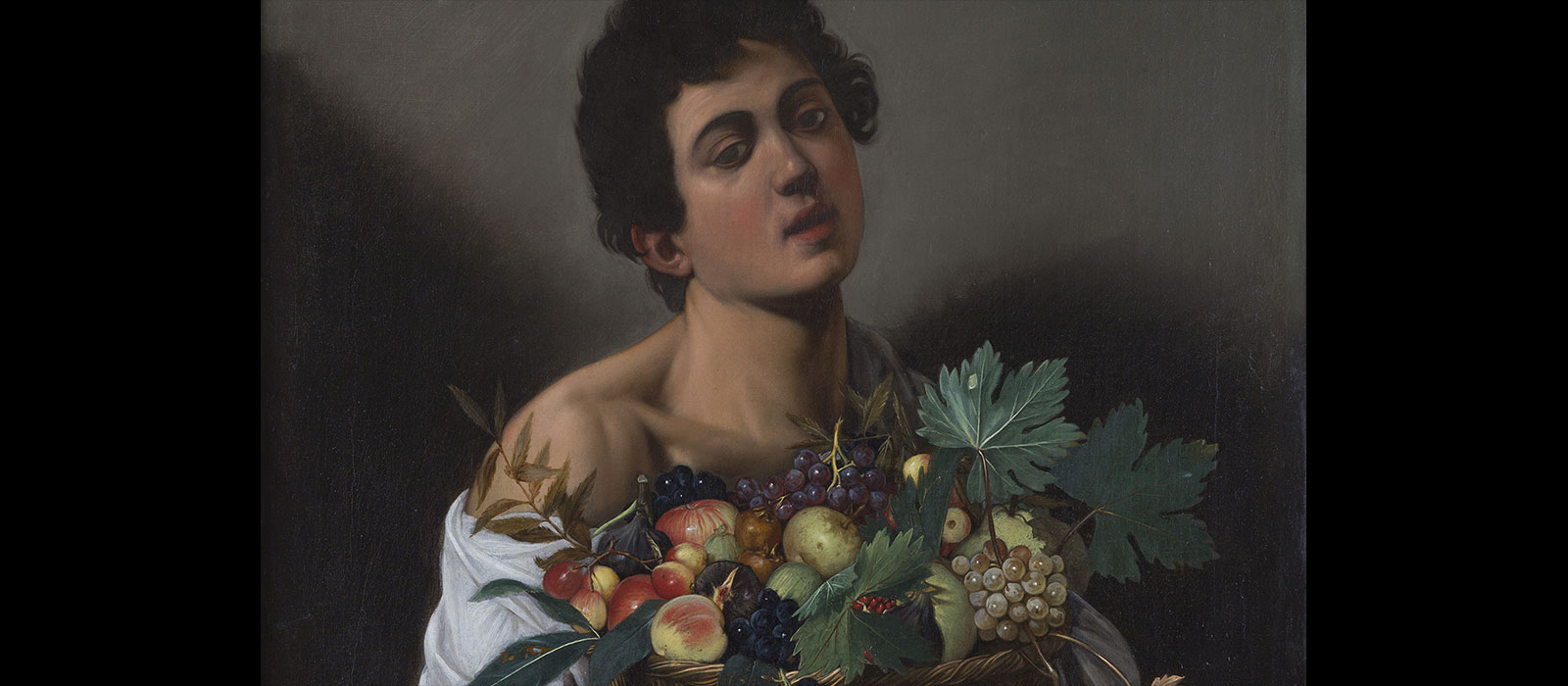 Portrait of a young male with dark hair holding a basket containing grapes, apples, and leaves.