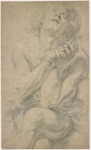 Young man sitting down with hands clasped held up in from of him and legs crossed.