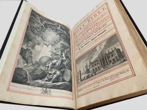 A large open book in front of a light grey background showing a full page sized image on the left and a title page on the right. The black, white and grey frontispiece on the left depicts a religious scene with angels and cherubs at the top and a holy light shining down on a man looking upwards in a rocky crag. The title page contains black and red text and a black, white, and grey engraving of a pillared building. The text above this image reads The Holy Bible containing the Old Testament and the New: Newly translated out of the Original Tongues and with the former translations diligently compared and revised by His Majesty’s special command. Appointed to be read in Churches. Below the image is text giving information about the printer and publication.