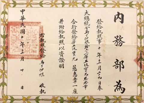 A horizontal rectangular document with a floral border composed of yellow flowers and green leaves linked together. There is black chinese script written vertically across the document with a red square stamp on the left side.