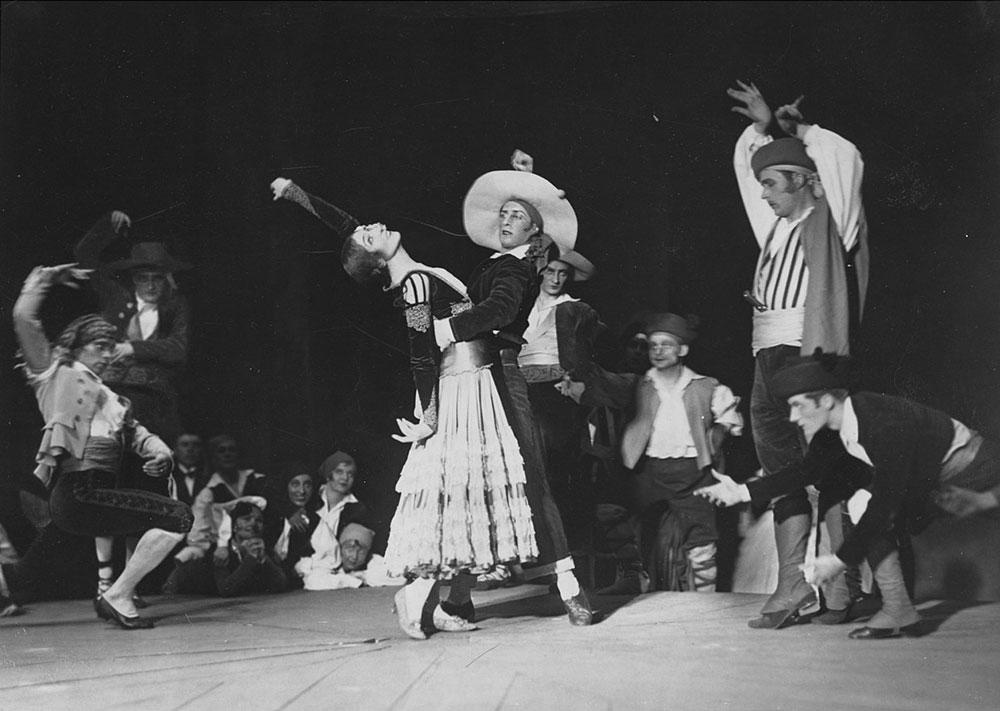 Black-and-white photograph of performers on stage in costume dancing.