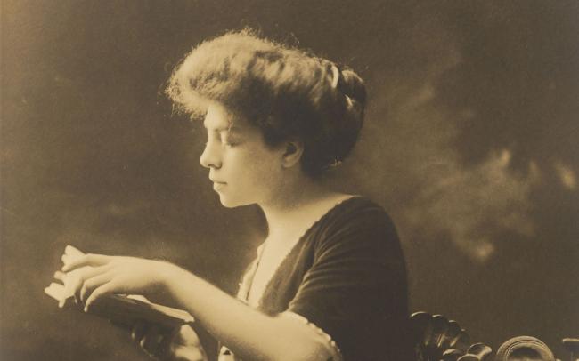 Sepia tone photograph of Belle da Costa Greene sitting and reading a book.