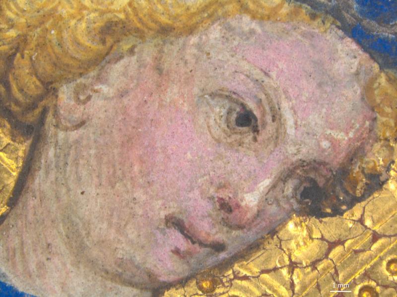 A micro-detail of a painted face shows pale, pinkish skin, golden curly hair, and a dark eye looking upwards. Blue paint is visible on the left, and cracked gold leaf is on the right. A 1 mm scale bar is in the bottom right corner.