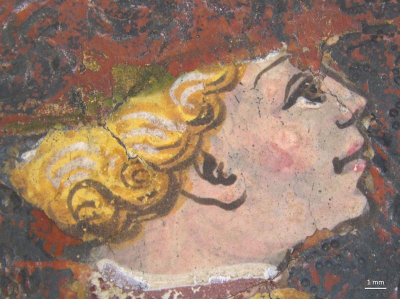 A close-up of a painted face in profile, looking right, with light-colored skin and curly blonde hair outlined in dark brown. The paint surface is cracked, revealing areas of red and dark brown around the face. A 1 mm scale bar is visible in the lower right corner.