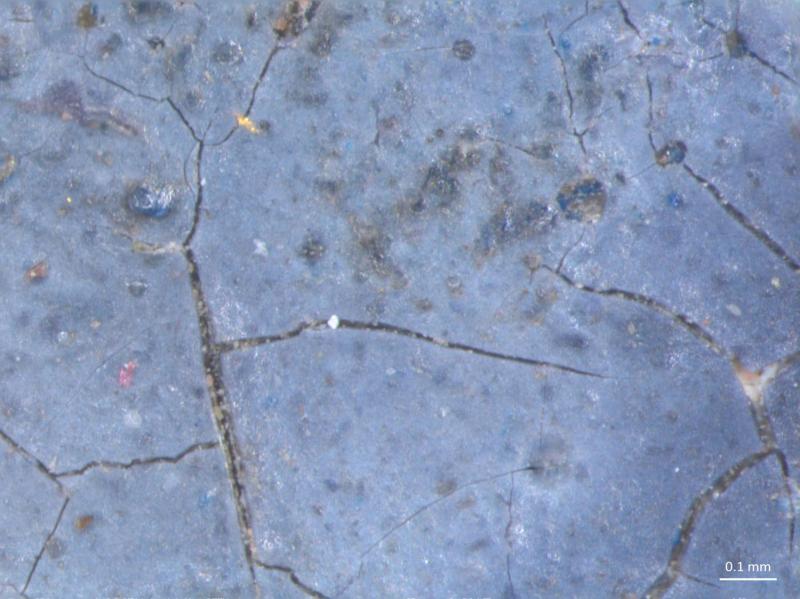 A microscopic image of a blue-gray surface covered in a network of fine cracks. A scale bar in the lower right indicates 0.1 mm.