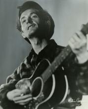 Black and white photograph of Woody Guthrie playing the guitar.