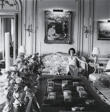 Black and white photograph of Jayne Wrightsman sitting on a couch in her Manhattan apartment surrounded by art objects.